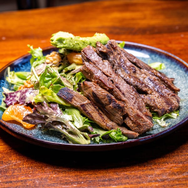 Grilled steak slices on a bed of mixed greens with avocado, walnuts, and mandarin oranges.
