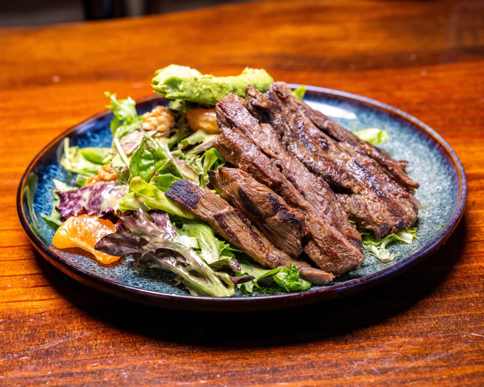 Grilled steak slices on a bed of mixed greens with avocado, walnuts, and mandarin oranges.