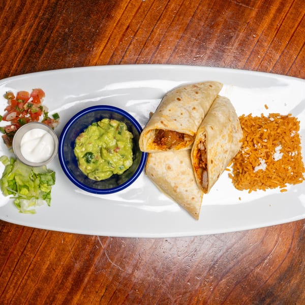 Two burritos with rice, guacamole, sour cream, pico de gallo, and lettuce on a white plate.