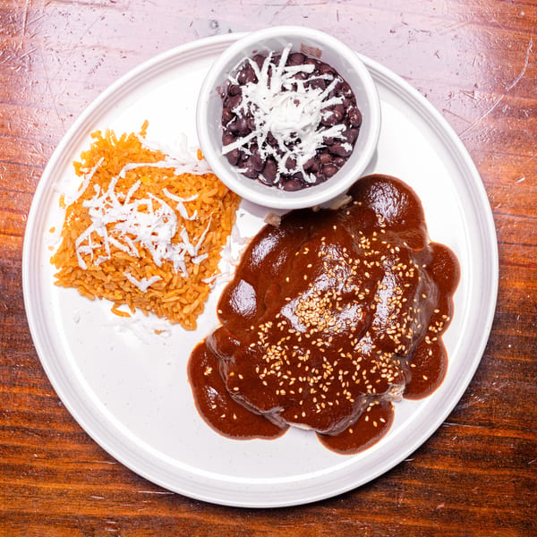 Chicken mole with sesame seeds, red rice, and black beans with cheese on a white plate.