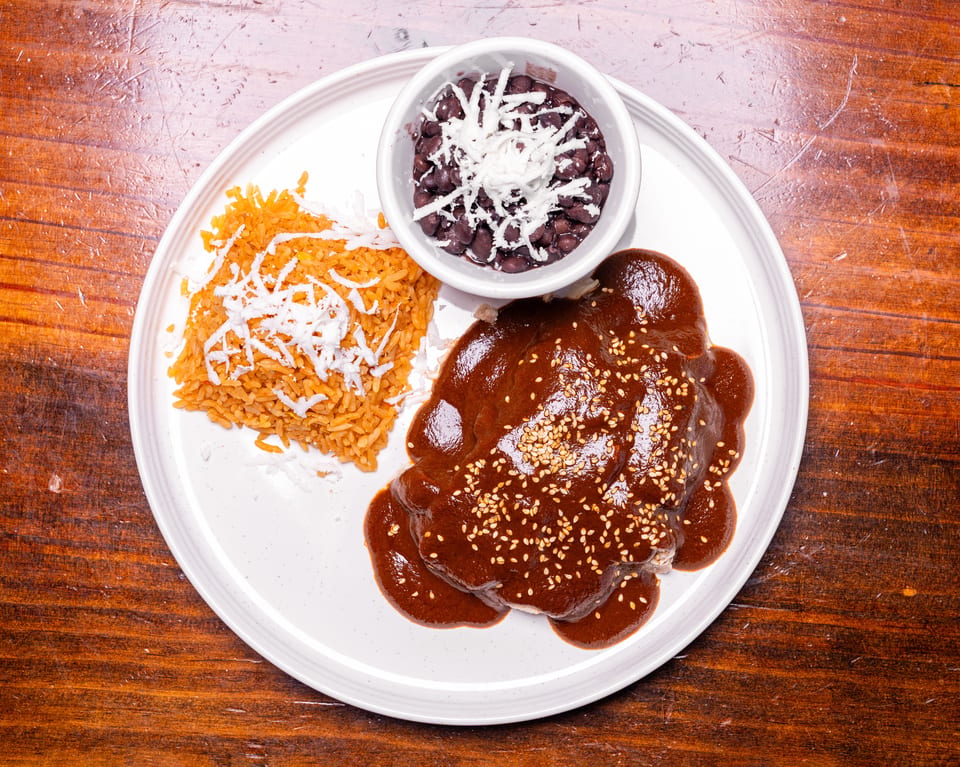 Chicken mole with sesame seeds, red rice, and black beans with cheese on a white plate.