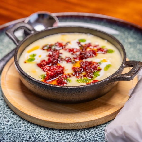 Creamy white dip with red and green garnishes in a black cast iron skillet on a wooden tray.