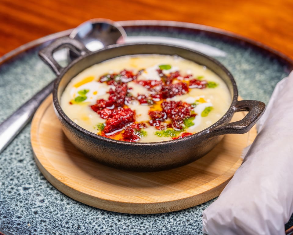 Creamy white dip with red and green garnishes in a black cast iron skillet on a wooden tray.