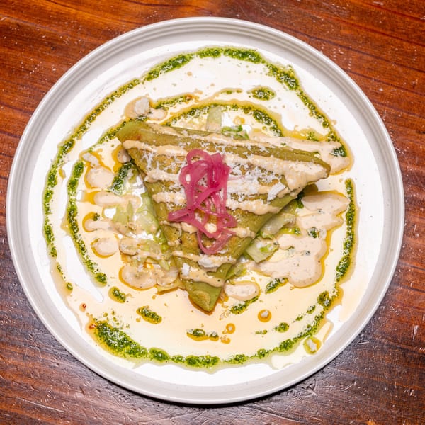 Green folded crepe topped with pickled red onions, sauce, and cheese on a white plate.