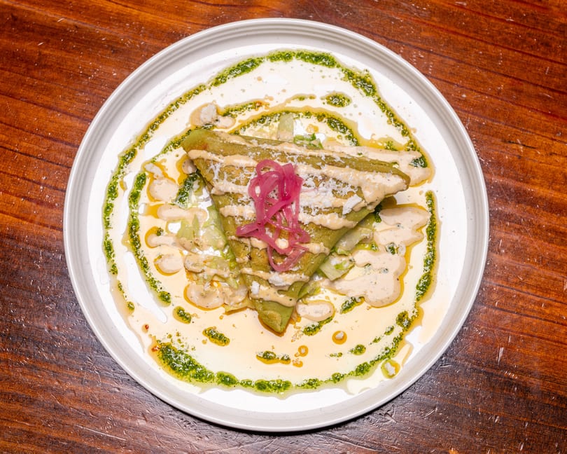 Green folded crepe topped with pickled red onions, sauce, and cheese on a white plate.