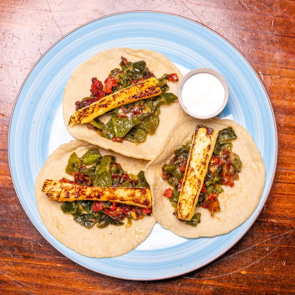 Three tacos with green and red filling, grilled cheese sticks, and a side of white sauce.