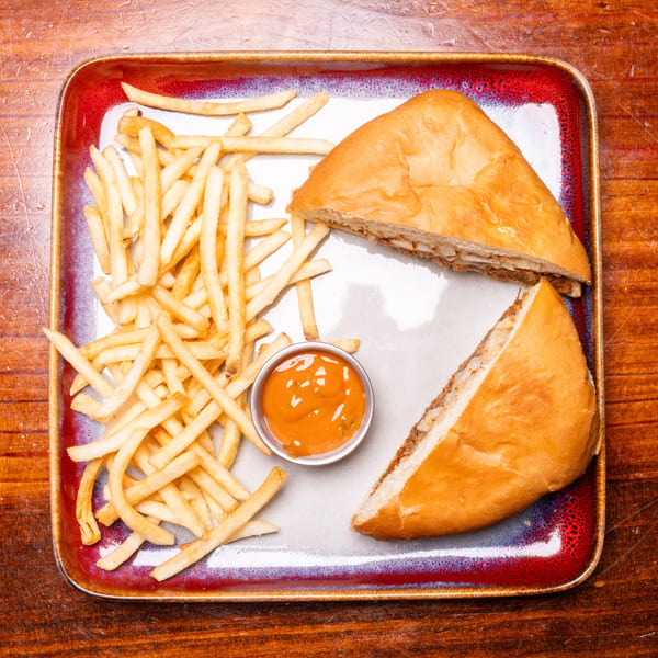 A calzone cut in half with a side of french fries and dipping sauce on a rectangular plate.