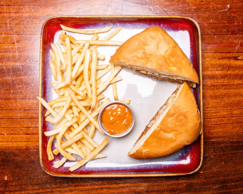 A calzone cut in half with a side of french fries and dipping sauce on a rectangular plate.