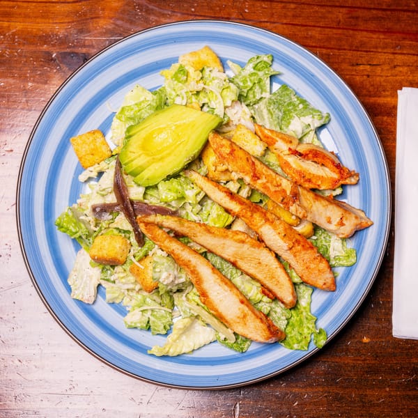 Caesar salad with grilled chicken, avocado, anchovies, and croutons on a blue striped plate.