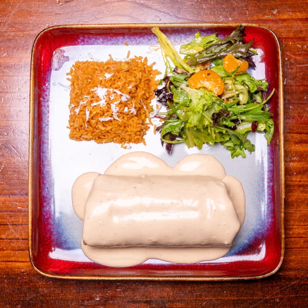 A burrito covered in creamy sauce, with a side of rice and a green salad with mandarin oranges.