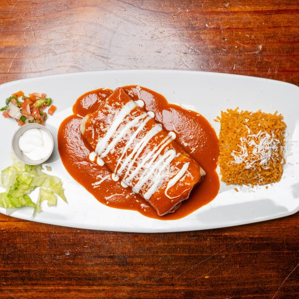 A burrito covered in red sauce and sour cream, with rice, salsa, and lettuce on a white plate.