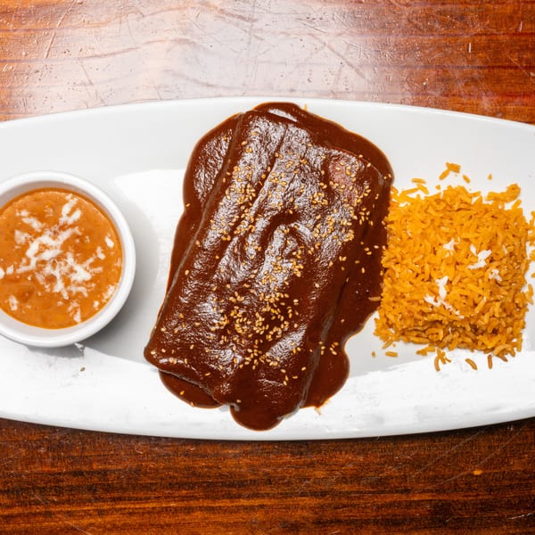 Enchiladas with mole sauce and sesame seeds, served with rice and a side of beans.