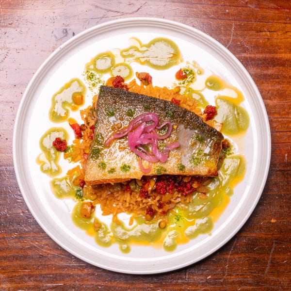 Crispy-skinned fish fillet with pickled onions, rice, red relish, and green sauce on a white plate.