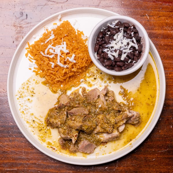 Pork in green sauce with rice and black beans, topped with cheese, on a white plate.